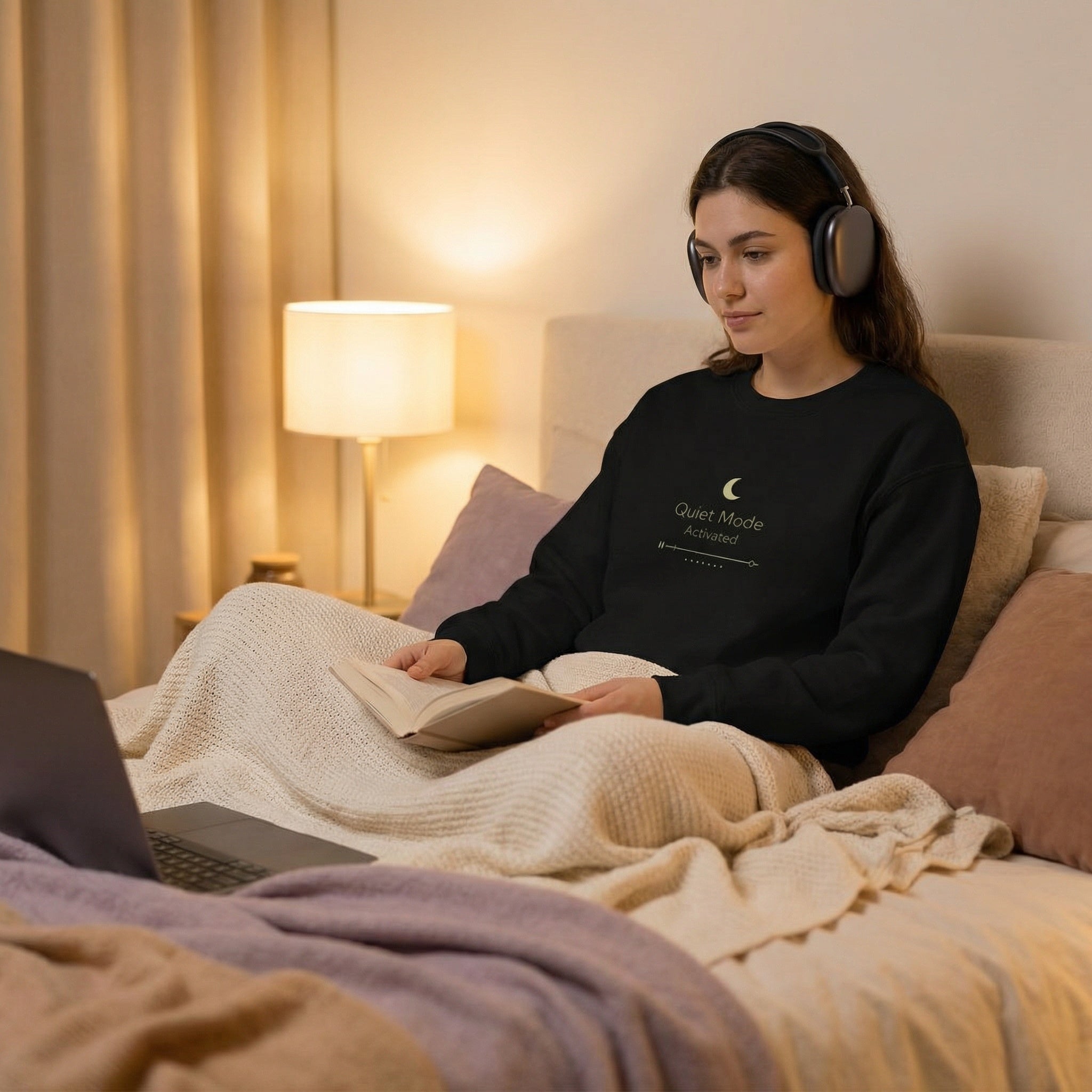 Woman reading a book with headphones on in a cozy bedroom setting.