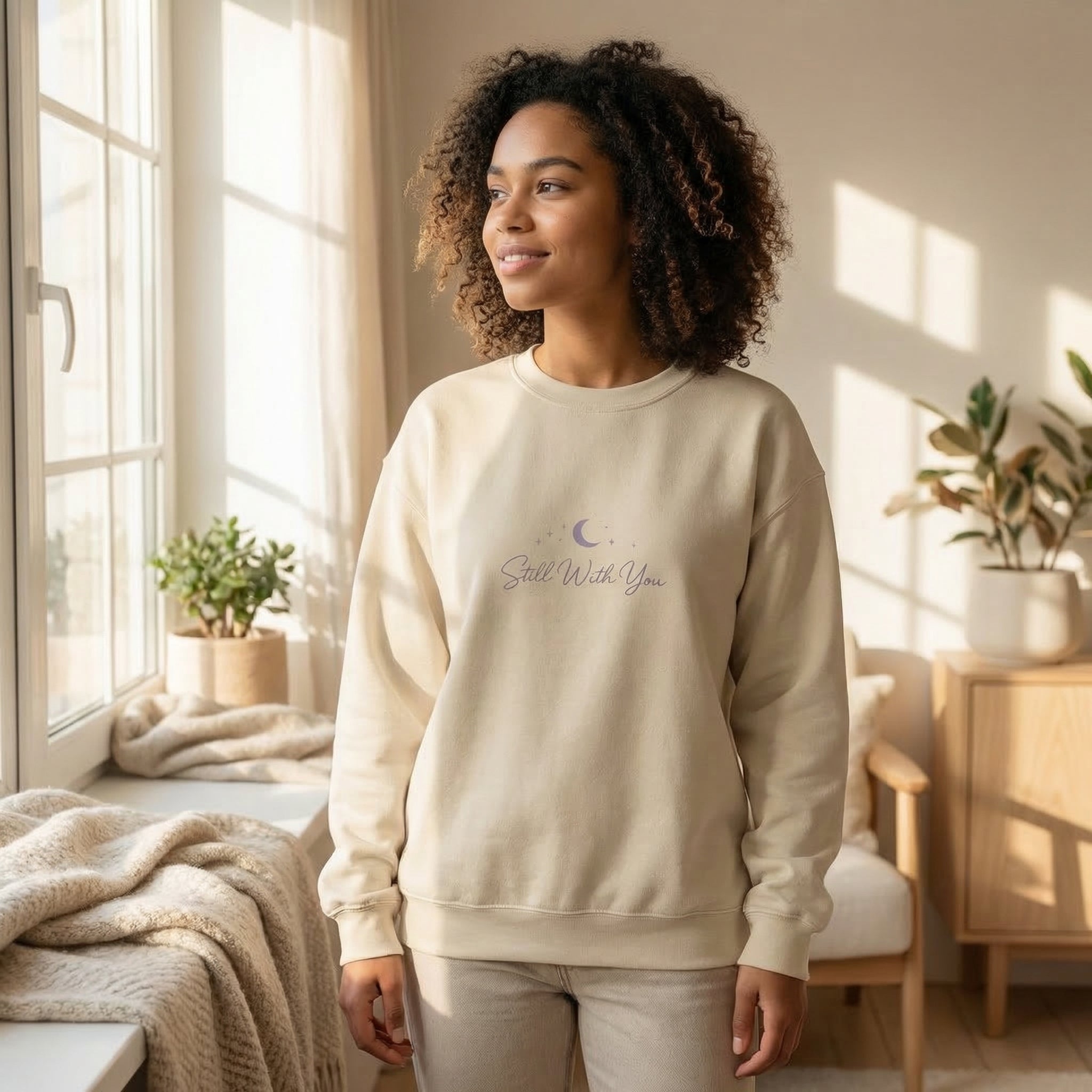 Woman wearing a beige sweatshirt with text and graphics in a bright room.