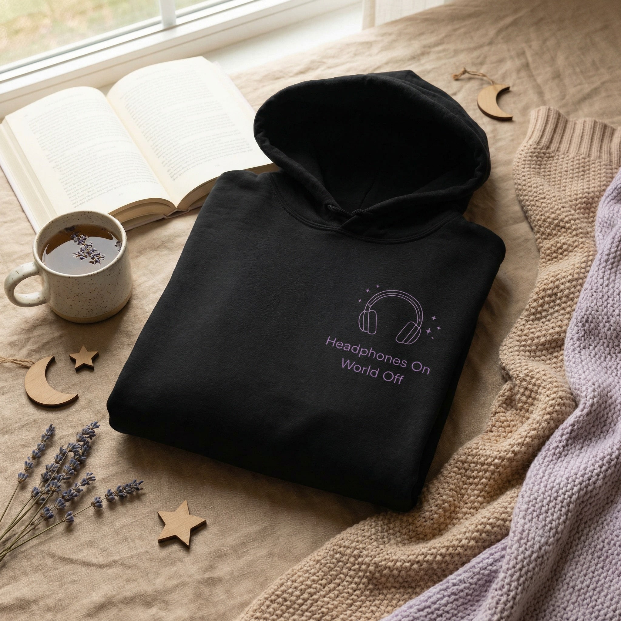 Black hoodie with 'Headphones On World Off' text on a textured surface with a cup of tea and lavender.