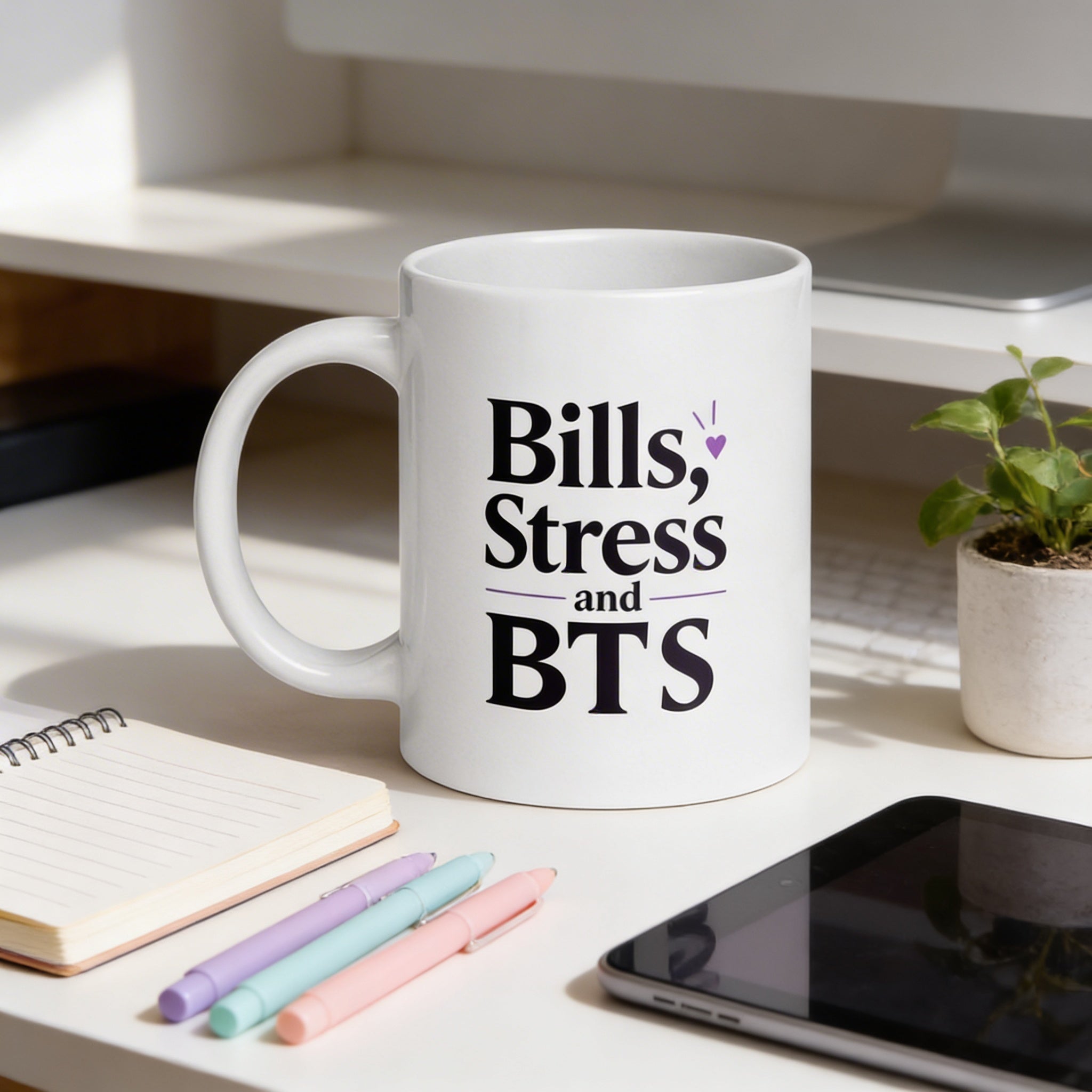 White mug with 'Bills, Stress and BTS' text on a desk with stationery items.