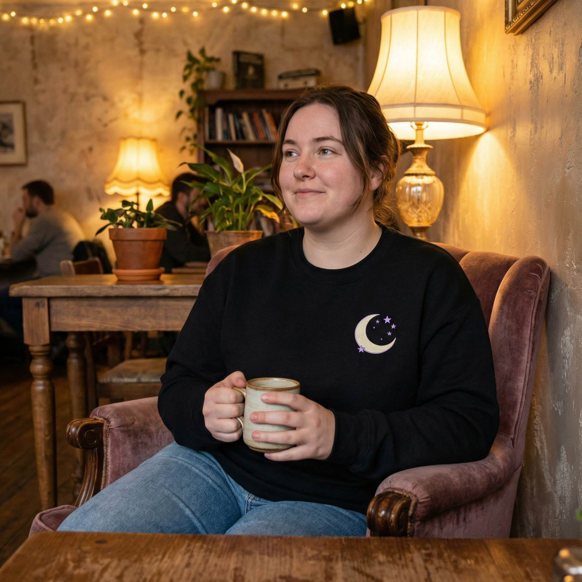 Woman sitting in a cozy cafe holding a mug, surrounded by warm lighting and decor.