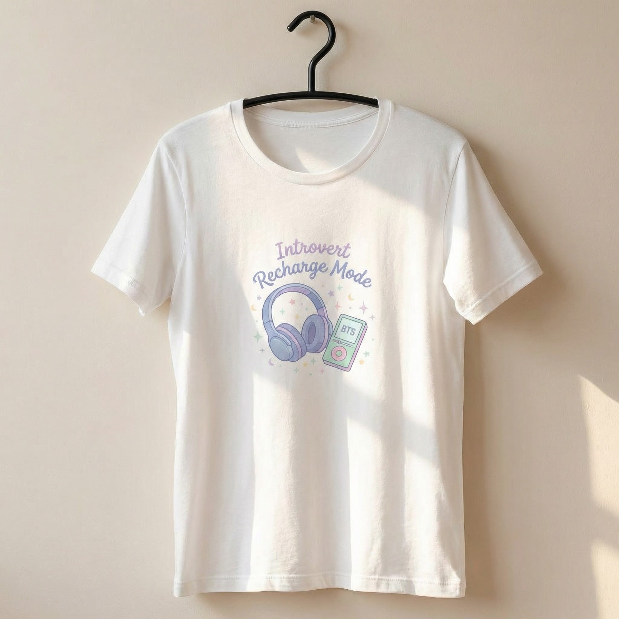 White t-shirt with 'Introvert Recharge Mode' design featuring headphones and a phone on a beige background